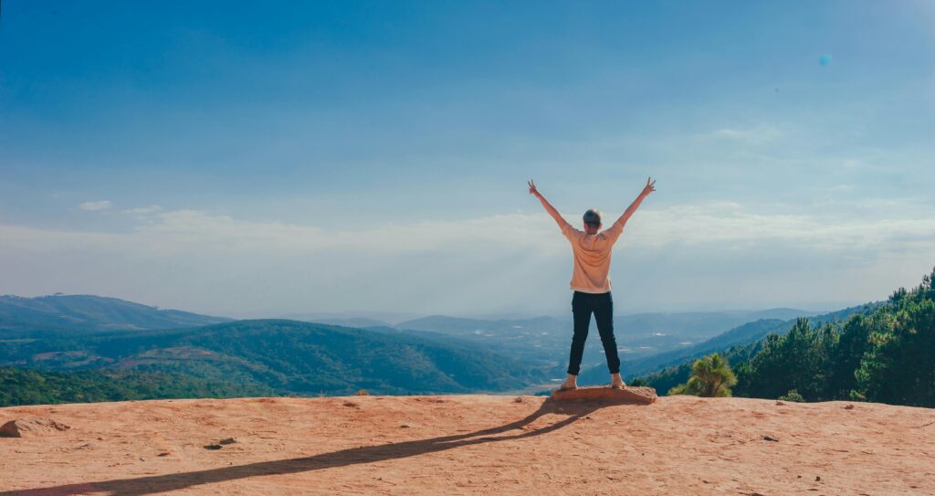 pexels-photo-1134188-1134188 A man raises his arms in triumph on a rocky mountain summit overlooking a vast landscape